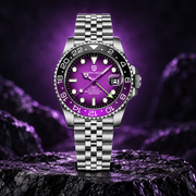 A stainless steel wristwatch with a vibrant purple dial and matching purple bezel markings, displayed on a dark rock against a purple-lit rocky background.