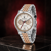 A Maserati chronograph watch with a silver and rose gold two-tone metal bracelet and a beige dial, displayed on a dark marble surface against a dark red background.